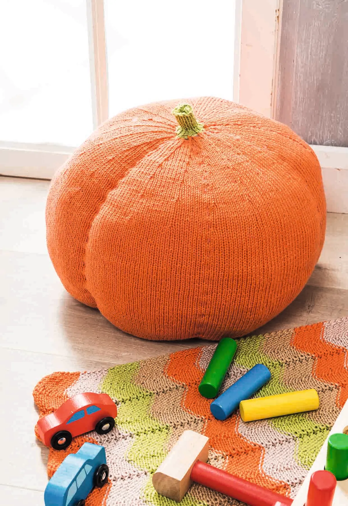 a big swishy orange knitted pumpkin squats on the floor surround by big crayon sticks. Comfy and fun!