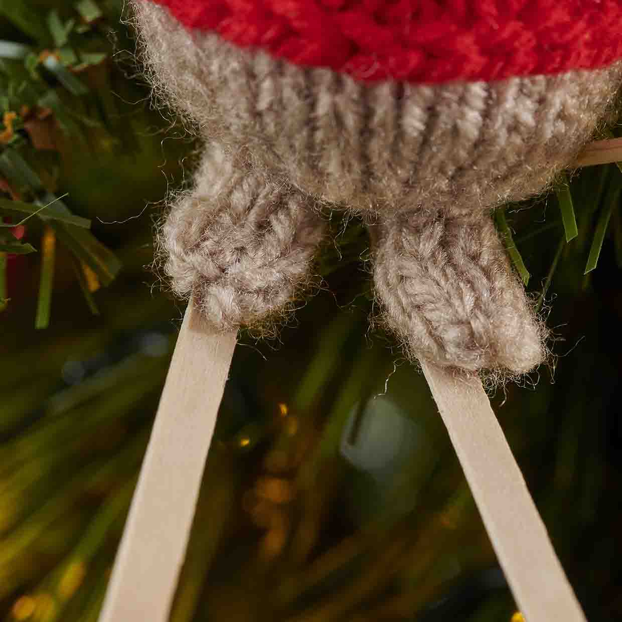 Close up of two knitted blobby pale brown feet glued on to two wooden coffee stirrers