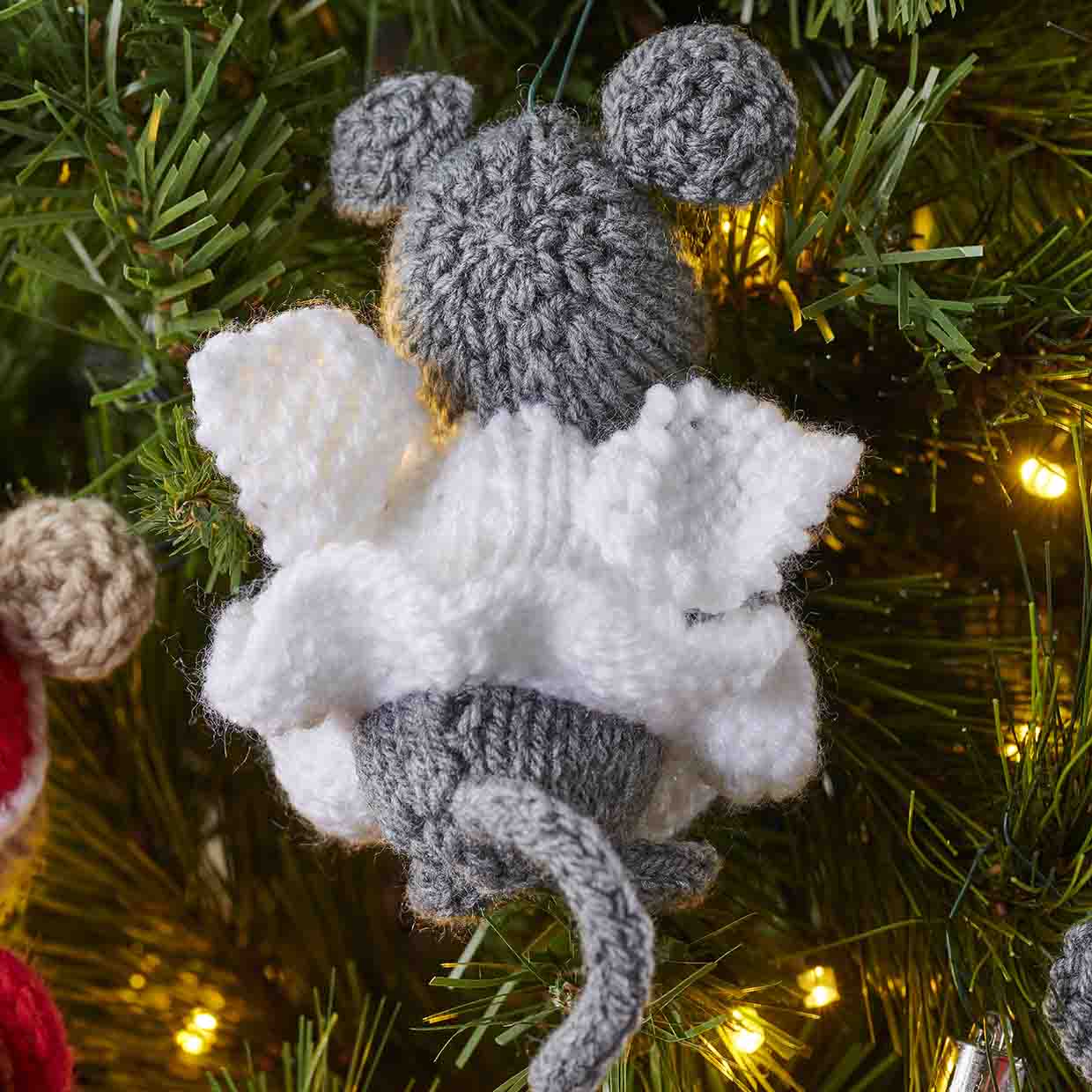 The Christmas mouse is dressed as a fairy and seen from behind so that her knitted wings attached to her body are seen and her long grey knitted tail