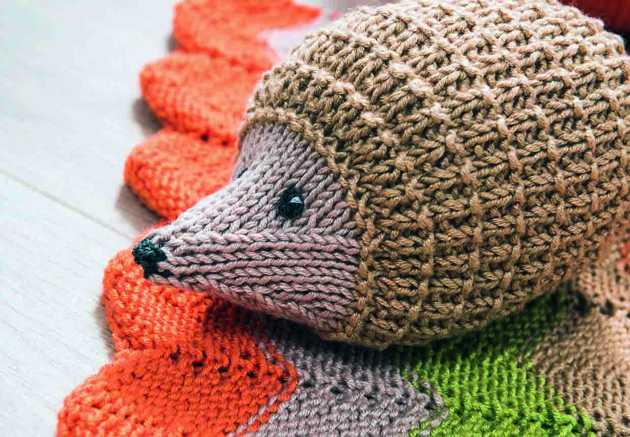 the knitted hedgehog is seen from the side. You can see the shaping on his head towards his pointy nose