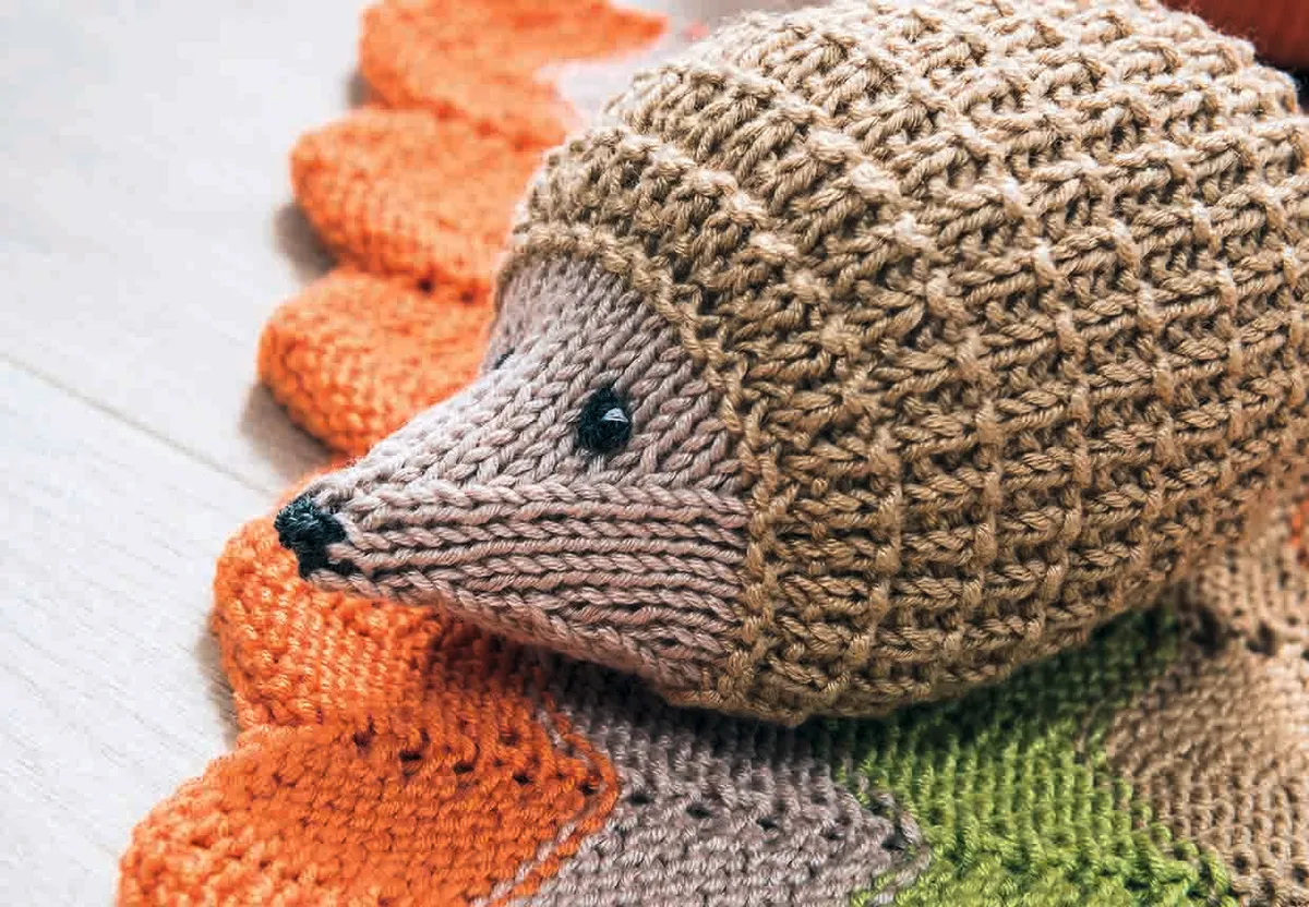 the knitted hedgehog is seen from the side. You can see the shaping on his head towards his pointy nose
