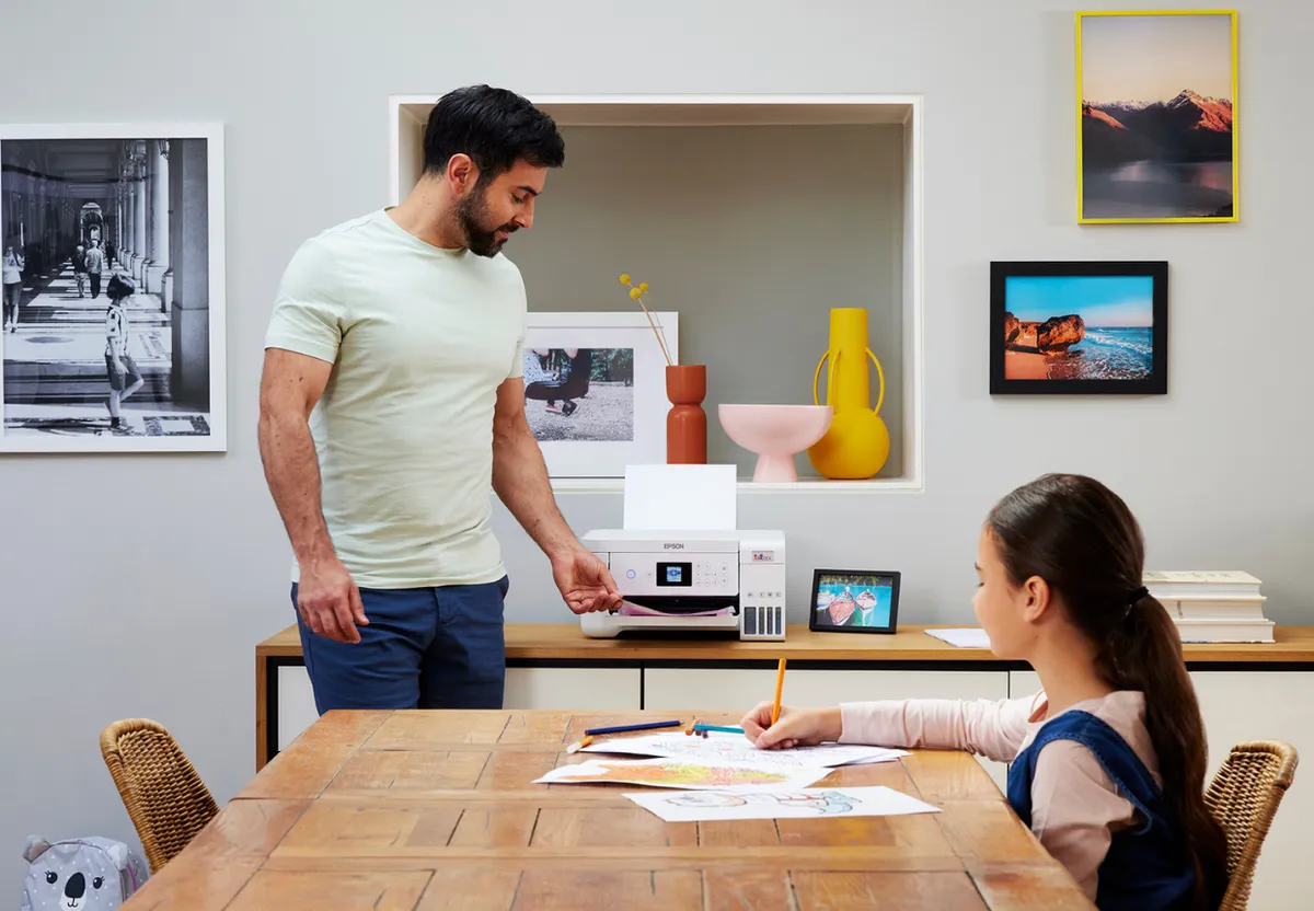 Father printing off pages on an EcoTank printer and his daughter drawing in the foreground