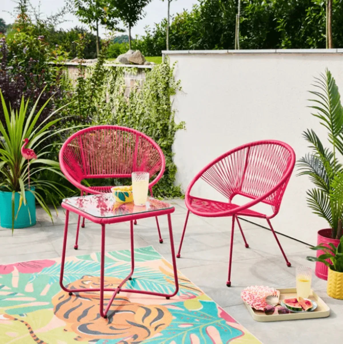 pair of bright pink string seats and a pink table in a small backyard with plants