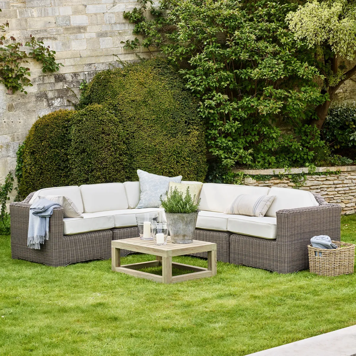 Large corner sofa in a garden with white cushions and throw pillows plus a coffee table with a plant