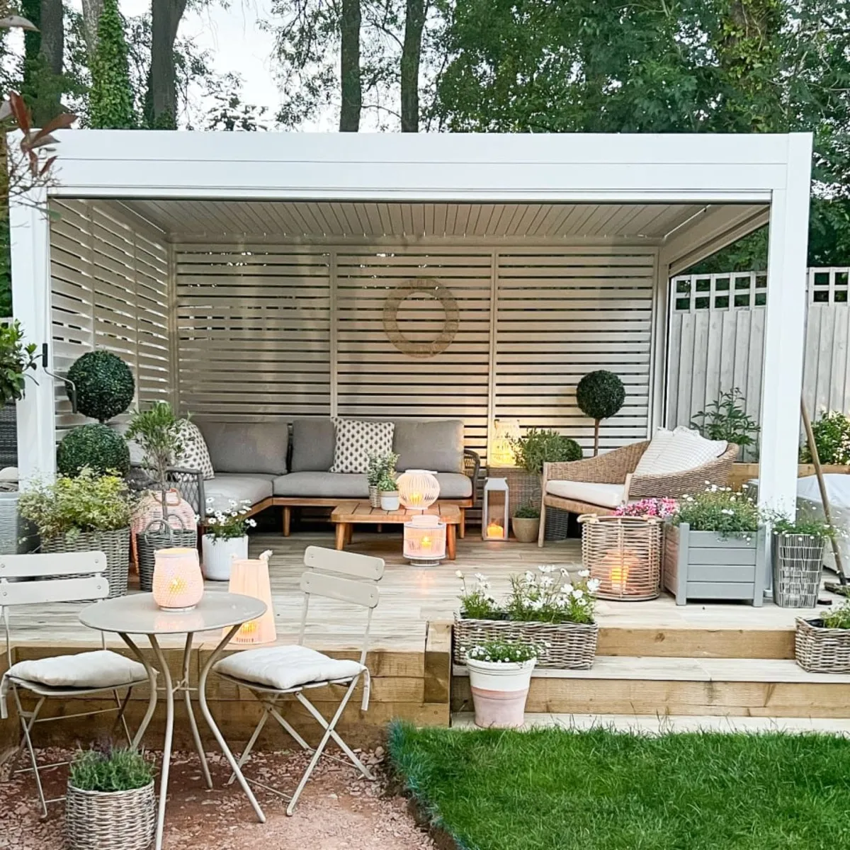 Large white pergola dressed with a corner sofa, chairs, lanterns and plants