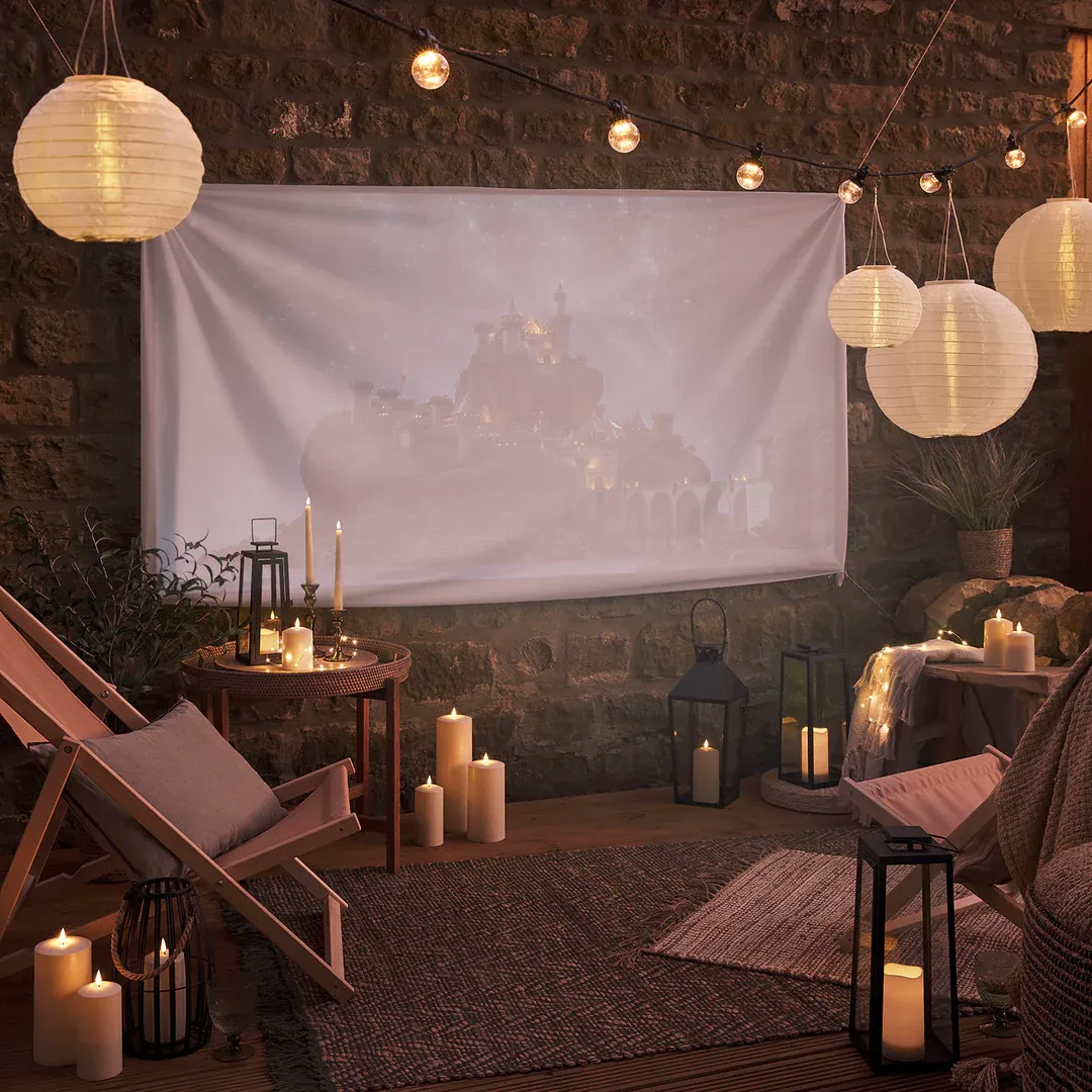 An outdoor movie night set up with chairs, candles, lanterns and festoon lights at night