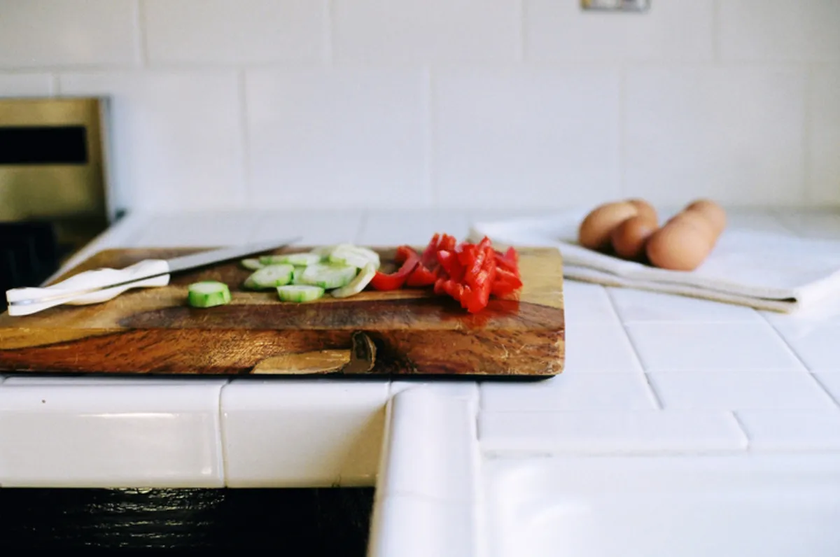 White tiled kitchen worktop with chopping board in the foreground with chopped red peppers and cucumber