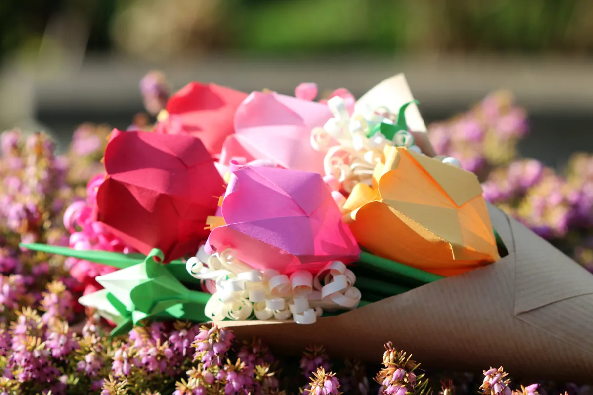 Origami flower bouquet wrapped in paper and laid on a bed of flowers