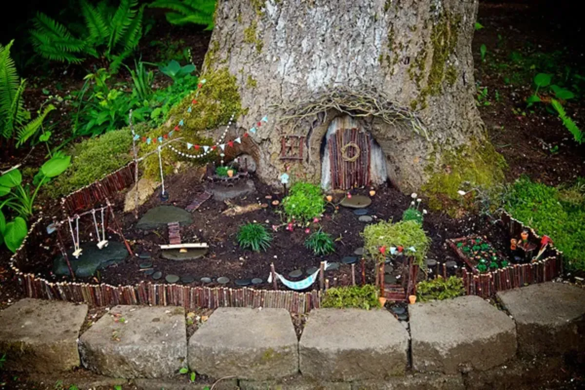 Magical fairy garden with a door set into a tree, a fence, bunting, hammock, swings and plants