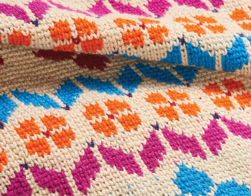 Colourful crochet rug with orange flowers and pink and blue motifs on a cream background