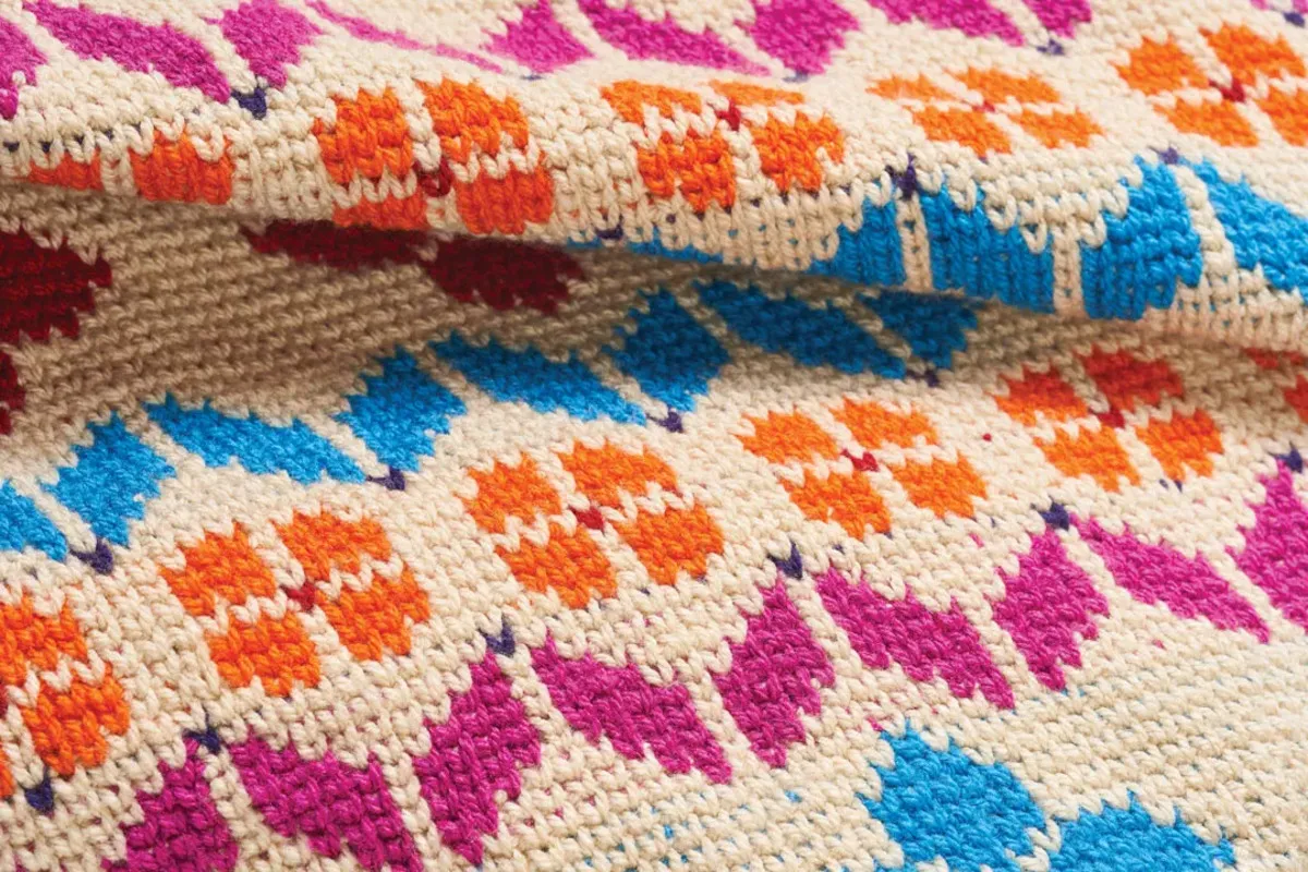 Colourful crochet rug with orange flowers and pink and blue motifs on a cream background
