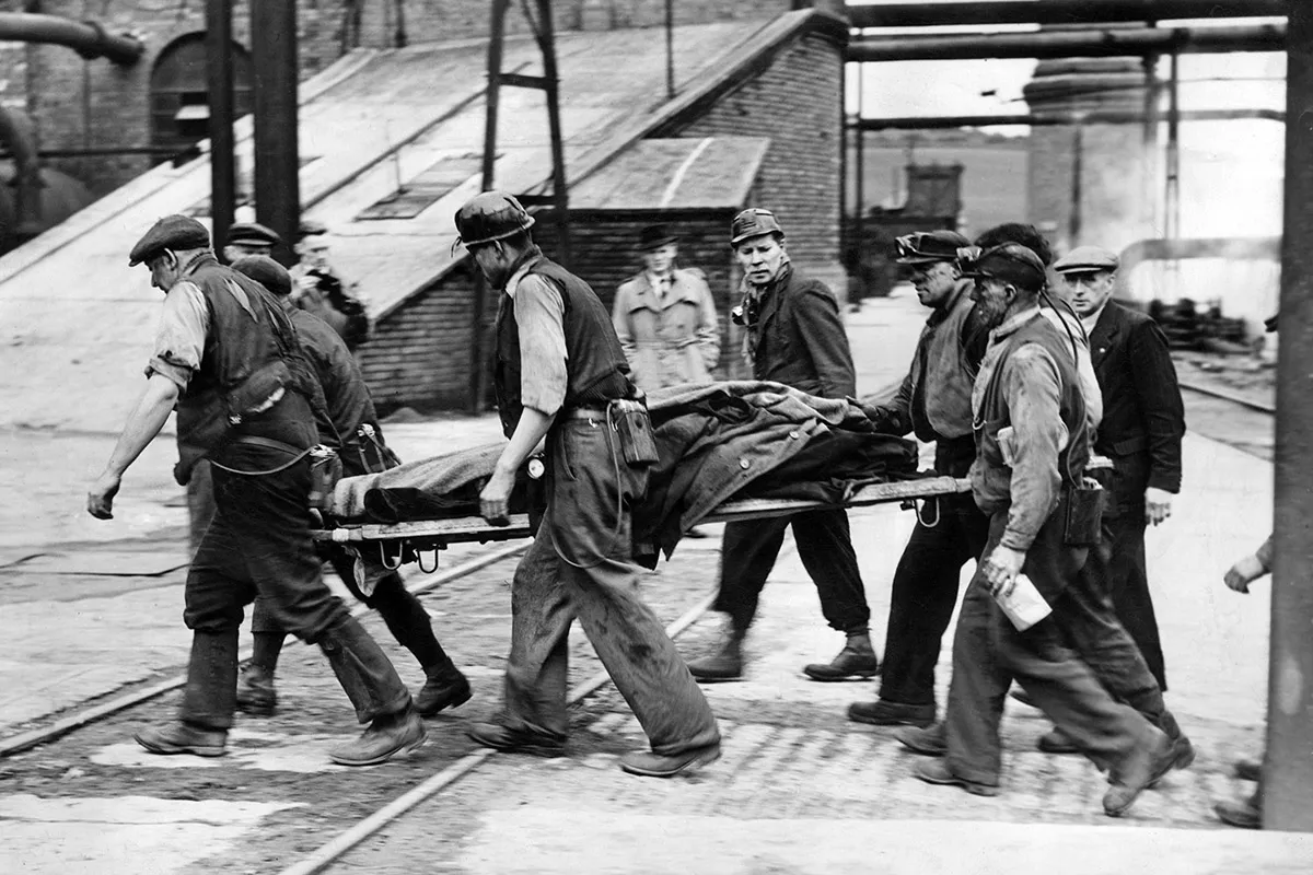 Black and white photograph of a group of coal miners carrying a man on a stretcher