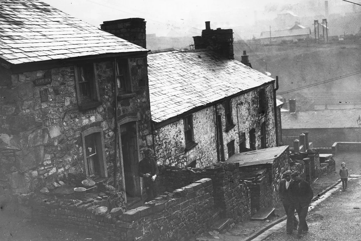 A black and white picture of a miner's cottage with a colliery behind it