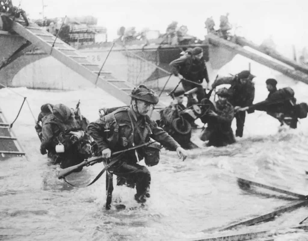 Black and white photograph showing soldiers descending from a battle ship into the surf at D-Day