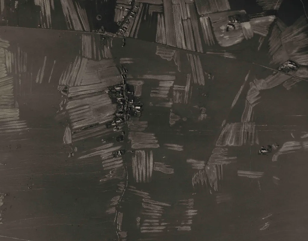 An extremely dark and primitive black and white aerial photograph, showing land divided into fields