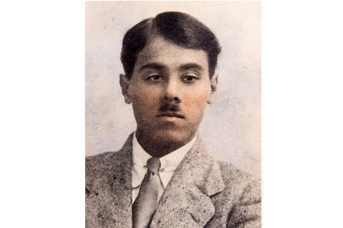 Colour tinted photograph from the 1920s of young Indian man with a toothbrush moustache wearing a suit with a grey jacket