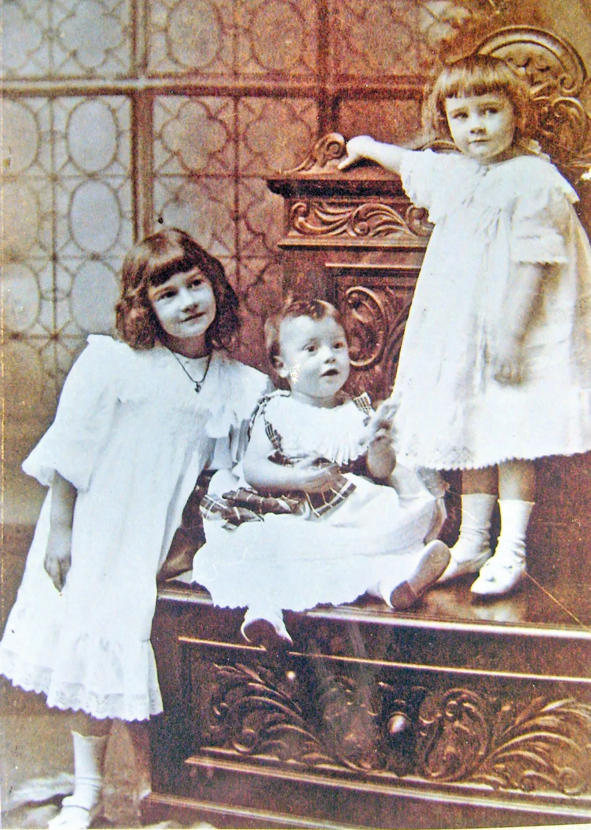 Black and white photograph of three children in old-fashioned white dresses