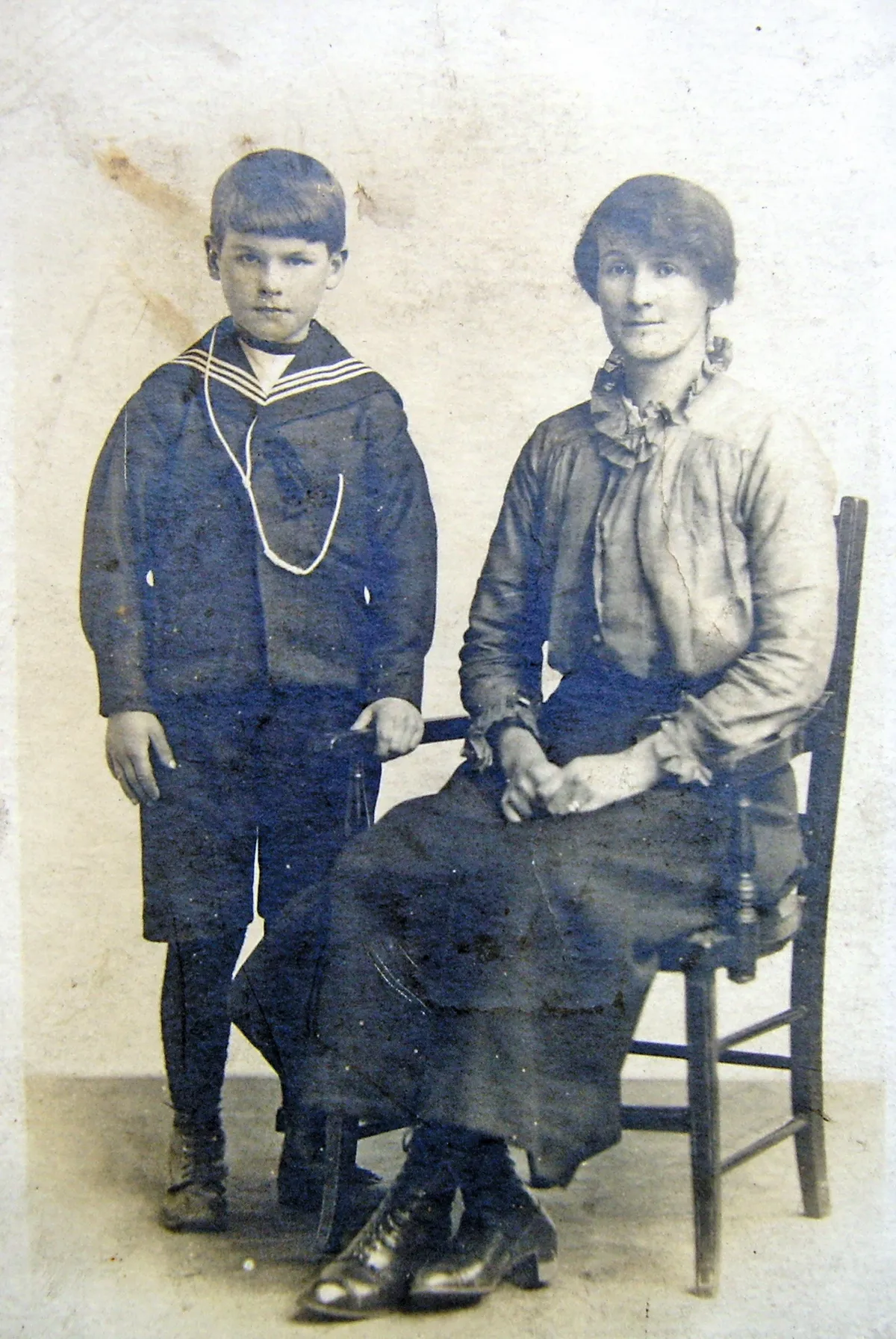Black and white photograph of a woman sitting on a chair and a little boy in a sailor suit