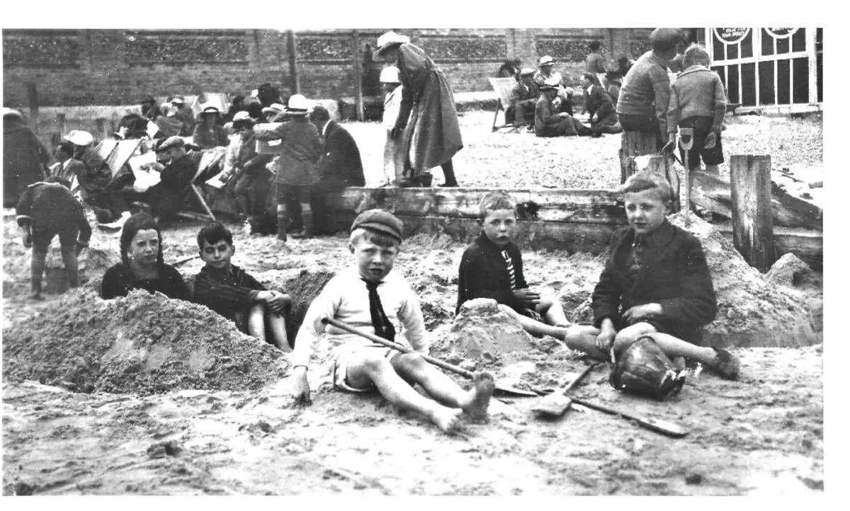 Black and white photograph of a group of children in old-fashioned clothing sitting on the beach
