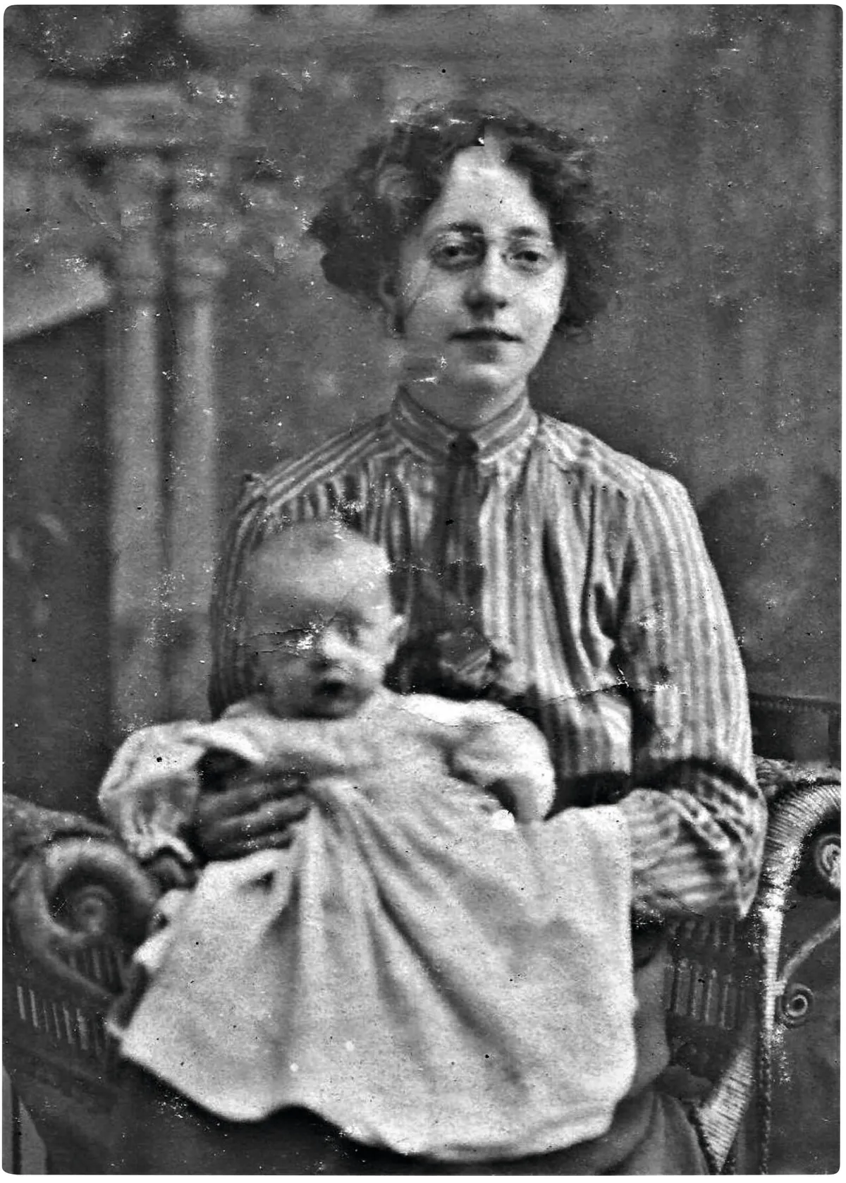 Black and white photograph of a young woman in Edwardian dress wearing spectacles and holding a baby