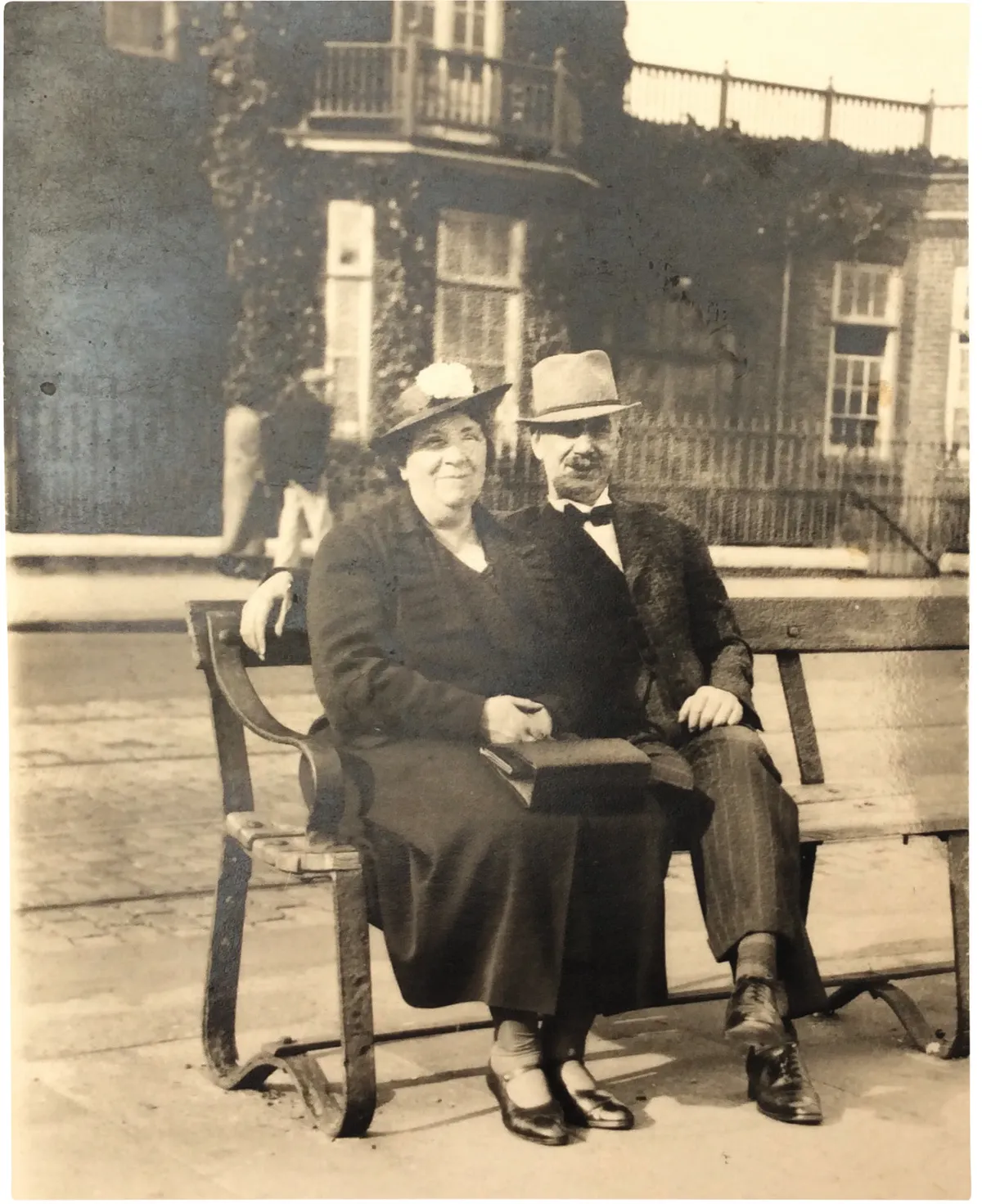 Black and white photograph of an older couple in old-fashioned clothes sitting on a bench
