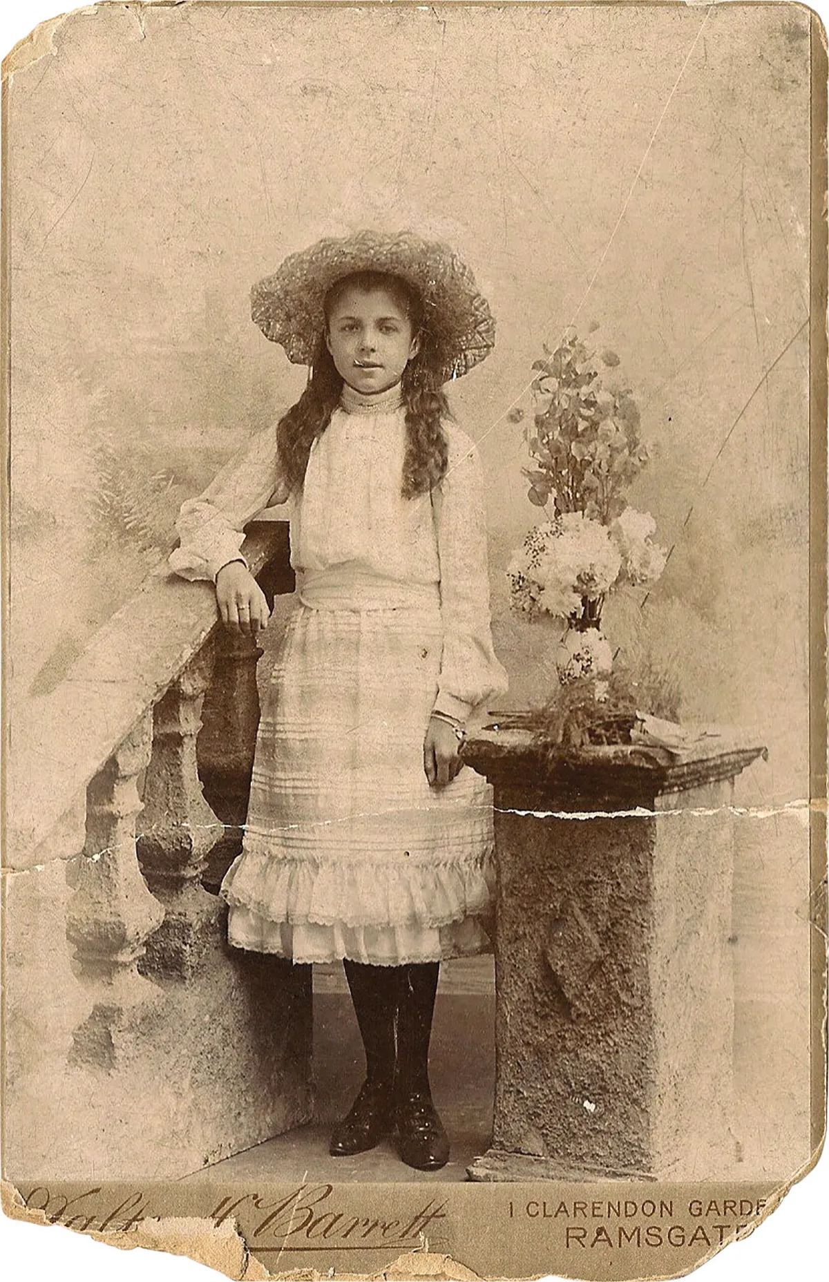 Black and white photograph of a little girl in a white Victorian dress and sunhat