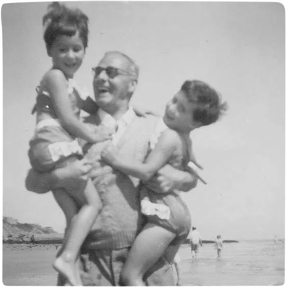 Black and white photograph of a man laughing and holding twin little girls at the seaside