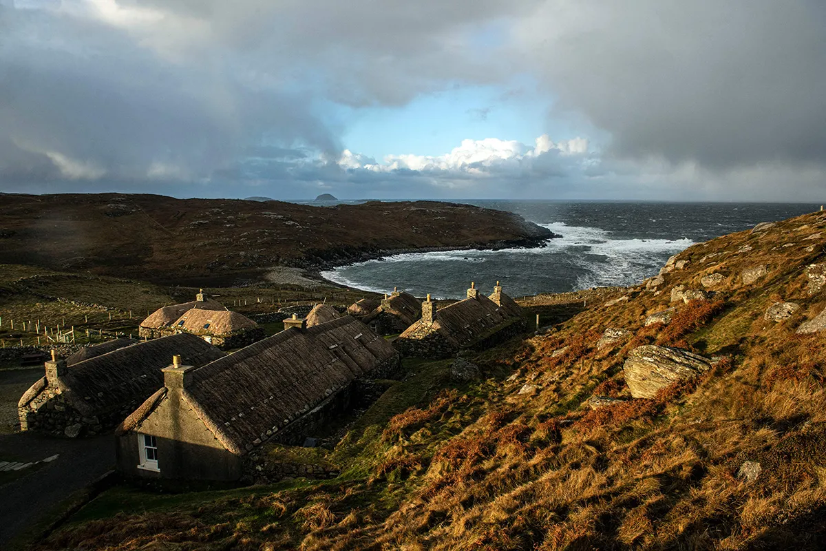 Colour photograph of thatched cottages by the sea on a Scottish isle