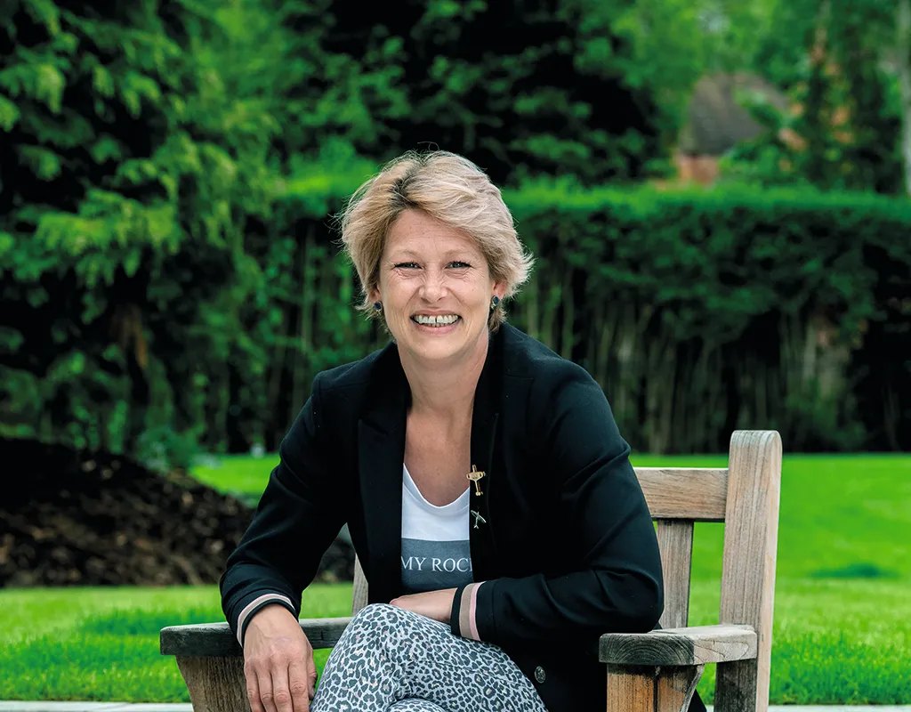 Colour photograph of a woman with short blonde hair sitting on a bench in a garden