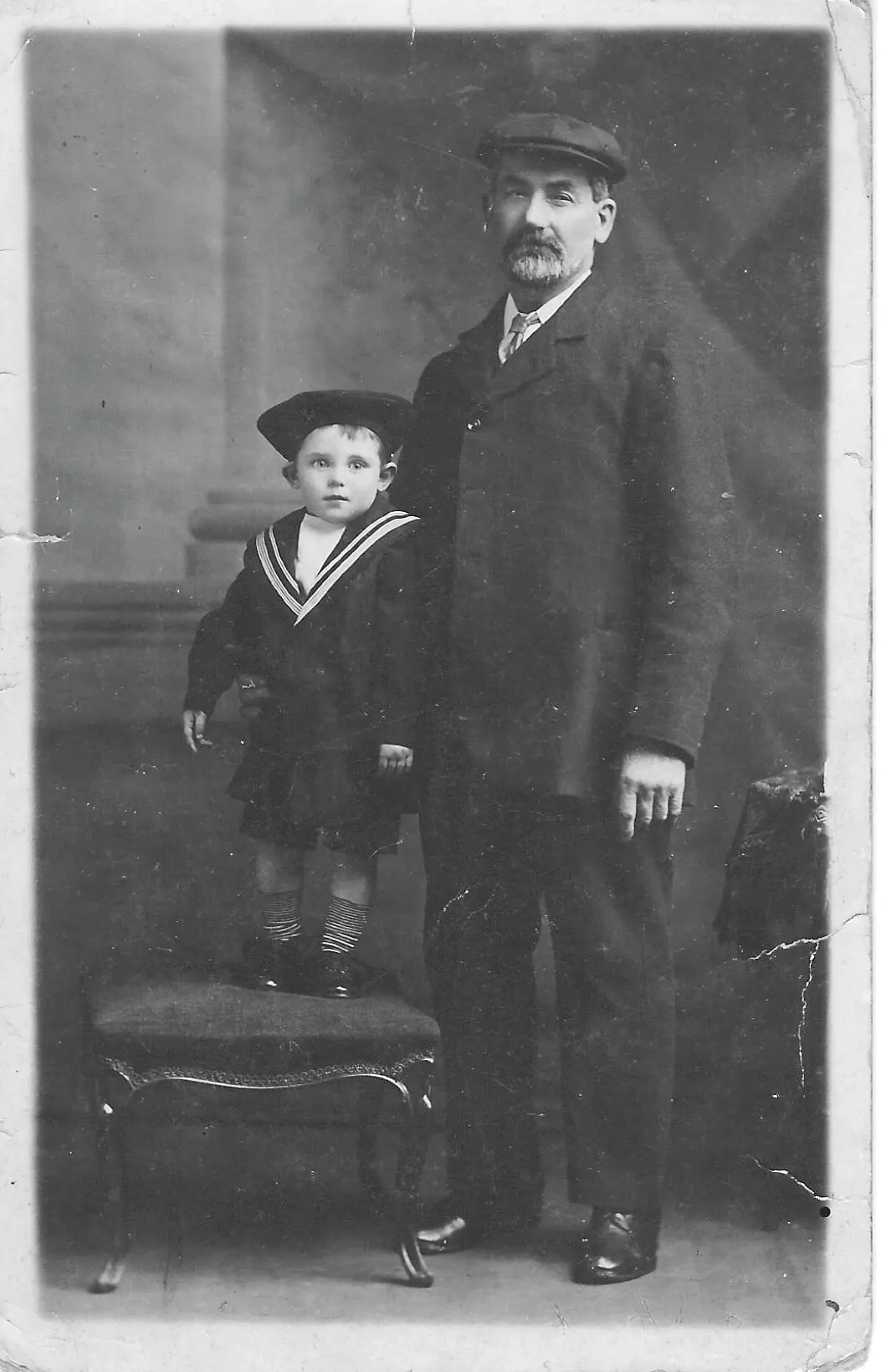 Black and white photograph of a man with a flat cap, moustache and beard and a little boy in a sailor suit