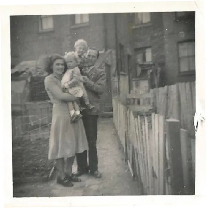 Black and white photograph of a couple holding two young children standing in the front garden