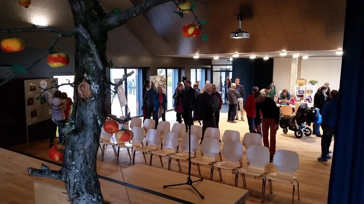 20181103_152154 Der Buechwäid-Saal dient als Sing- und Theatersaal. , Der Buechwäid-Saal dient als Sing- und Theatersaal. , Auch die Tagesstrukturen finden im Saal Platz., Zur Saaleinweihung wurde beim alten Sodbrunnen gleich auch noch eine Rotbuche gepflanzt., Zur Saaleinweihung wurde beim alten Sodbrunnen gleich auch noch eine Rotbuche gepflanzt., Kinder halfen mit, die Buche einzupflanzen., Im Obergeschoss der ehemaligen Turnhalle ist eine Medienraum eingerichtet worden., Die Aussenverkleidung der ehemaligen Turnhalle ist nun in Holz gehalten. , Die Aussenverkleidung der ehemaligen Turnhalle ist nun in Holz gehalten.