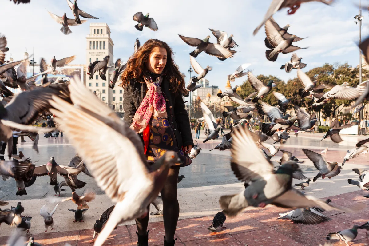 Young woman in the middle of a flock of pigeons in Barcelona