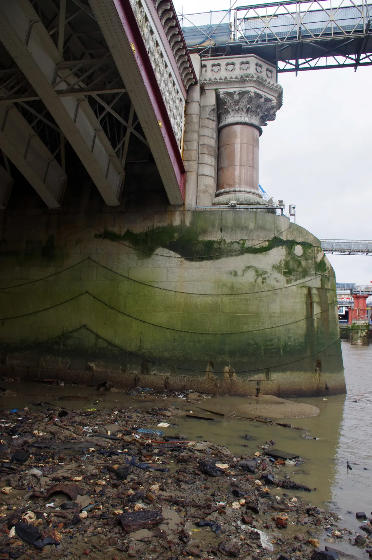 Pylon of Blackfriars Bridge at low tide on the River Thames, foreshore strewn with rusted metal, plastic, building rubble and other trash. © Simon McGill/Getty