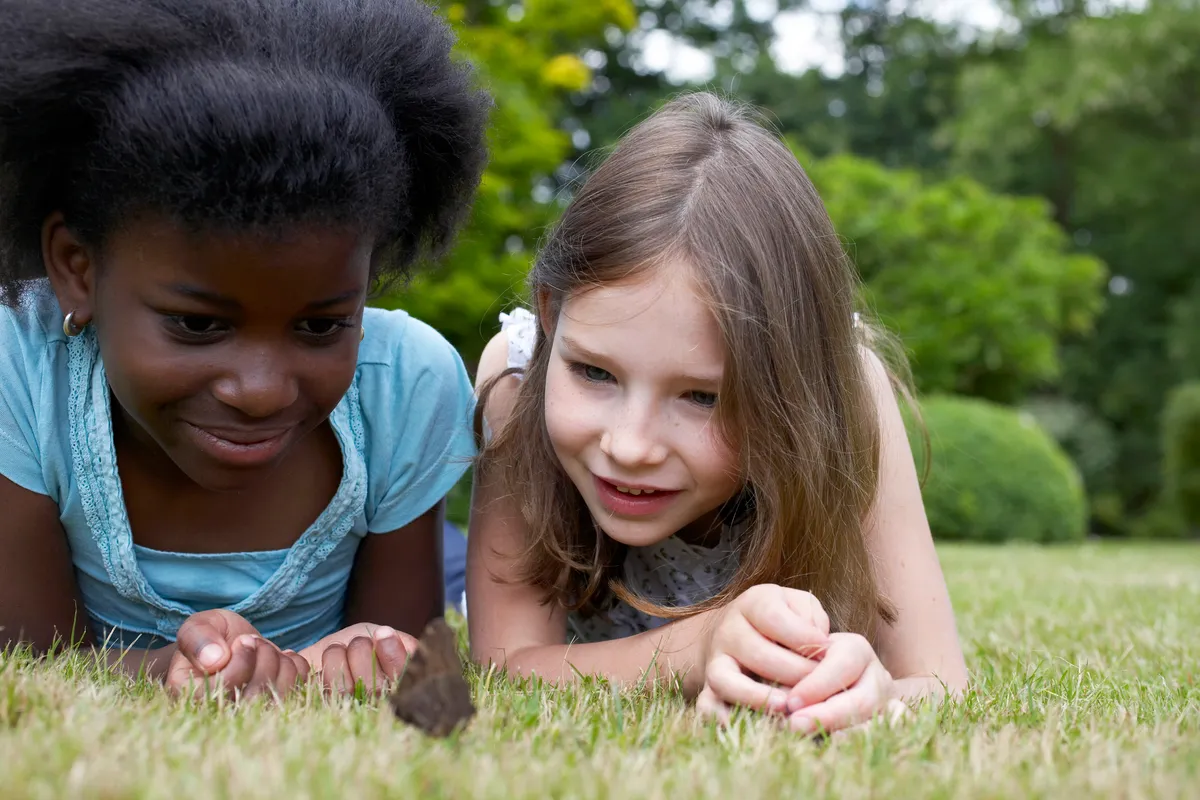 Two girls watching a butterfly in a garden. © Tim Hall/Getty