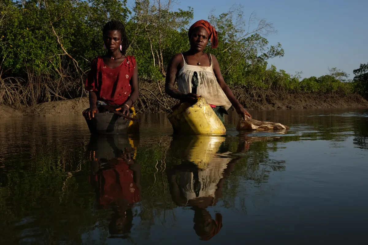 Environmental Balance in the Bijagos: A portrait of Ndira and Teresa of the Bijagos community in Guinea-Bissau, West Africa, who are part of a women's group who wade through water amidst the mangroves during low tide to look for oysters. The oysters are then sold or sometimes used in traditional ceremonies. © Ricci Shryock, Guinea-Bissau