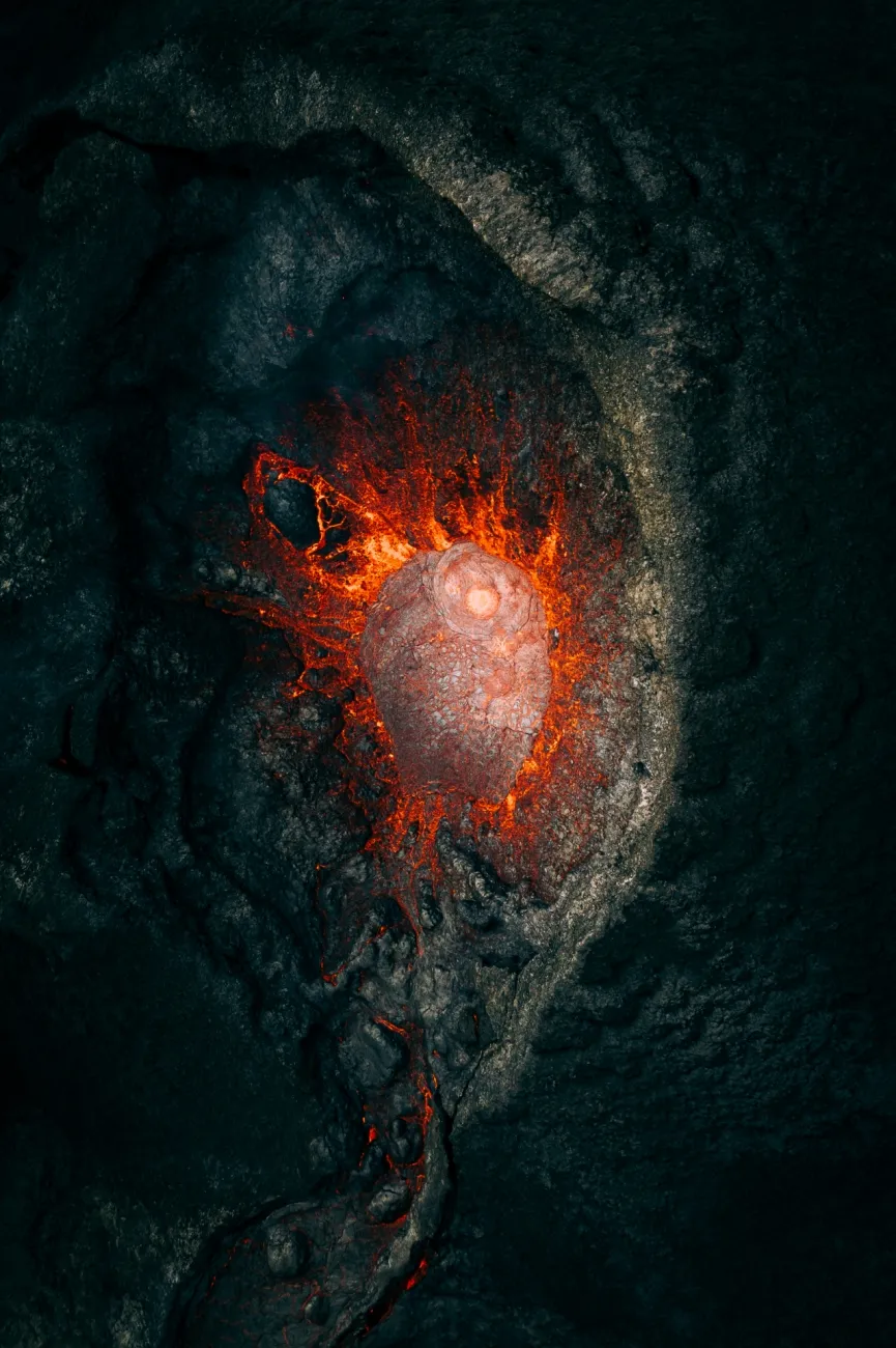 Aerial view directly into the mouth of a volcano; orange-red lava fills the centre of the image, surrounded by darker rock.