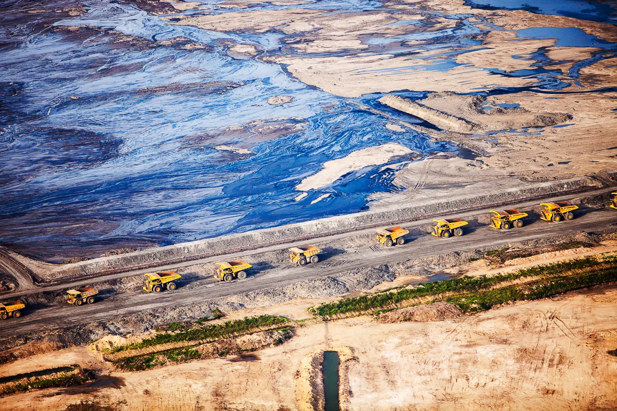 Massive dump trucks queuing to load with tar sand in front of a toxic wasteland. Syncrude mine, Athabasca, Alberta, Canada, 2012. Of all man’s efforts to exploit fossil fuels, the Canadian tar sands are by far the most environmentally destructive. The tar sands are a mix of bitumen, sands, clays and gravels. They are only economically viable to exploit when oil prices are at the higher end of their range. They can be turned into synthetic oil, but only by separating out the bitumen from the sands and gravels. At this site, deposits close to the surface are strip-mined. This involves clear-felling the boreal forest leading to a rate of deforestation second only to the rates in the Amazon rain forest. Each 2.5 square km of boreal forest supports 500 breeding pairs of migrant birds, as well as being home to Wolf, Lynx, Cougar, Black Bear, Grizzly Bear, Wolverine, Bison, Moose, Caribou, and Beaver. It is also an important carbon sink. In order to be able to separate the bitumen from the sands and gravels, the tar sand needs to be melted. This is achieved by forcing steam through the mix. The amount of gas used to make the steam means that the resulting oil has a carbon footprint up to three times that of conventional oil, making it a climate change disaster and when the steam condenses back to water, it contains many toxic pollutants from the bitumen. The wastewater is discharged into unlined tailings ponds that leach toxins out into the Athabasca River. These flow downstream and seriously impact the health of native Canadians living downstream. Rates of skin disease and rare cancers in these communities have risen steeply since the tar sands mining started. Mandatory credit: © Ashley Cooper / naturepl.com
