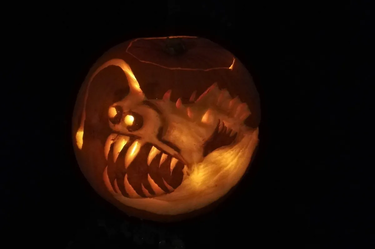 A pumpkin in darkness, lit up from within to show an anglerfish carving