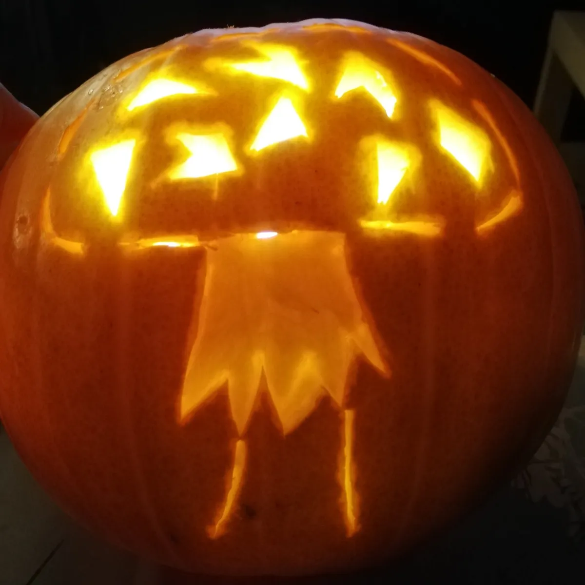 A pumpkin in the dark, lit up from within, showing a fly agaric carving in the pumpkin
