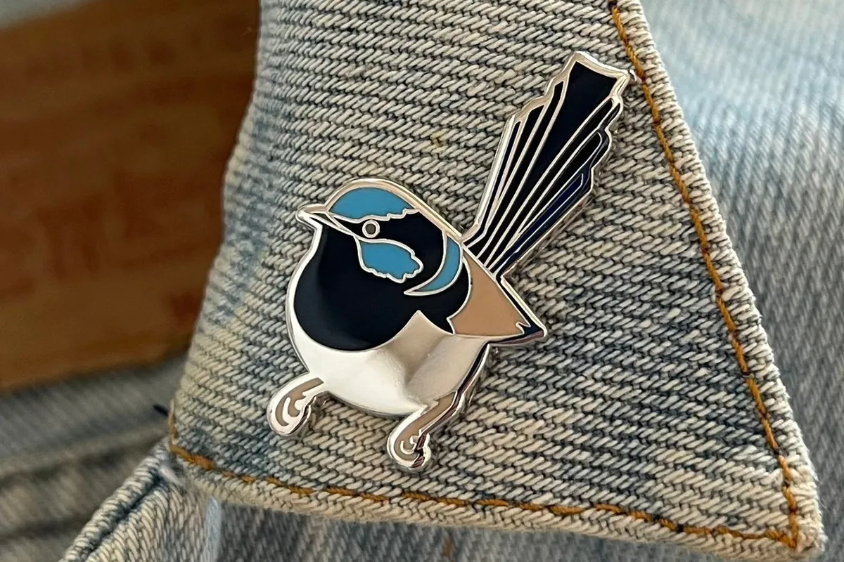 A superb fairy wren enamel pin with silver inlay, attached to a denim collar.