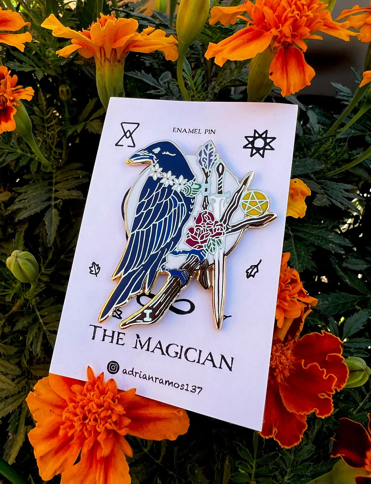 A raven enamel pin, with the raven as The Magician, perched on a branch with the four suits: Sword, Wand, Pentacle and the snail shell necklace serves as the Cup.