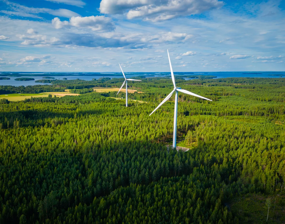 Aerial view of wind turbines in a forest next to a large lake in Finland on a sunny summer day