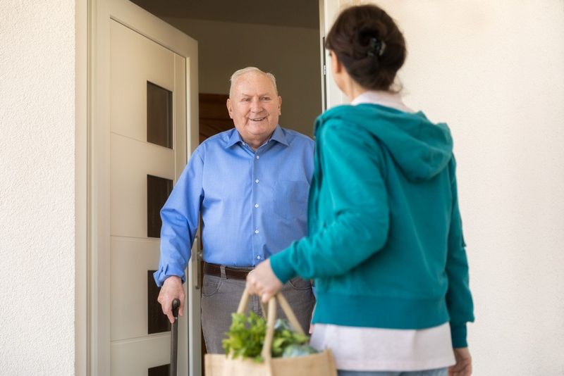 Eine Haushaltshilfe bringt einem Senior seinen Einkauf.Foto: FredFroese/E /Getty Images