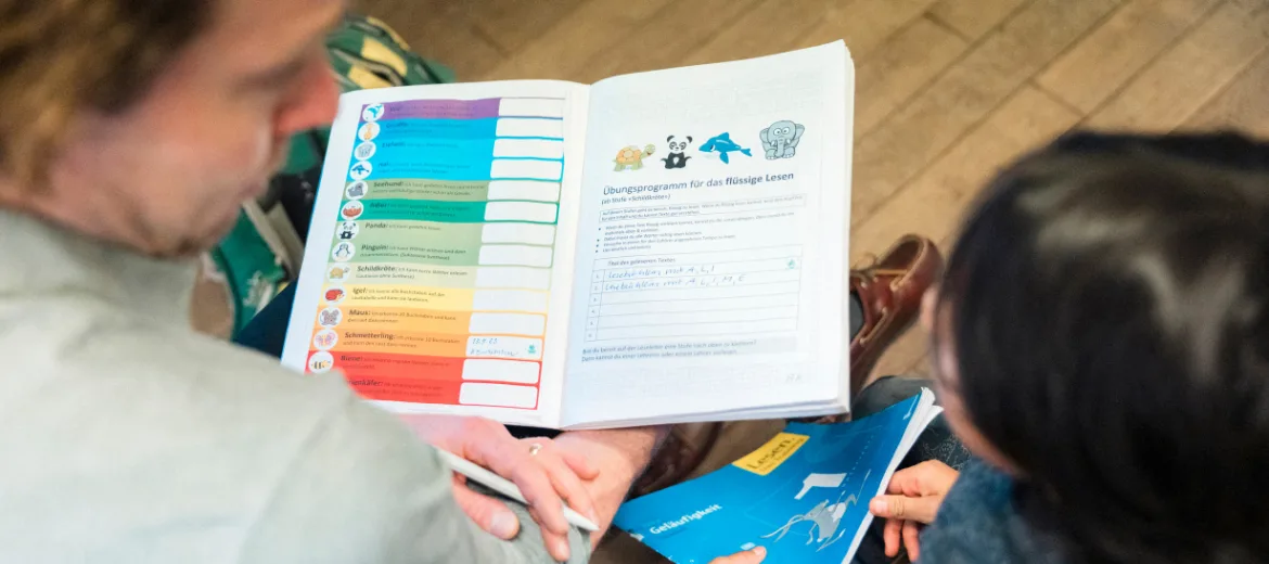 24-02-schulnoten-noten-alternativen-zur-note-hg Alternativen zur Note. Lehrer sitzt im Klassenzimmer mit Kind und bespricht dessen Leistung.