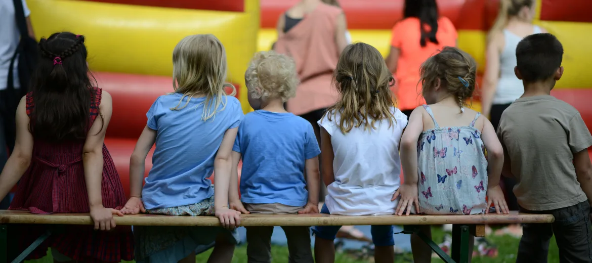 24-11-kinder-kinderrechte-metaversum-kurzgeschichte-schweizer-elternmagazin-fritz-und-fraenzi-hg Kinder sitzen auf Bank vor Hüpfburg