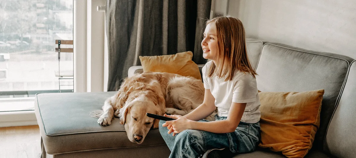 medien-srf-kids-schweizer-elternmagazin-hg Les médias. La fille regarde la télévision et s'assied sur le canapé avec le chien.
