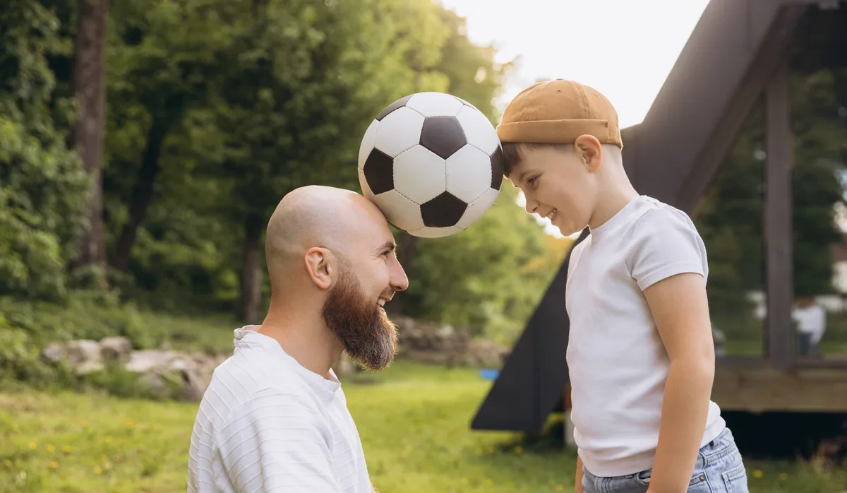 Father and son playing with soccer ball celebrating Father’s Day Eltern sein ist ein ein Balanceakt