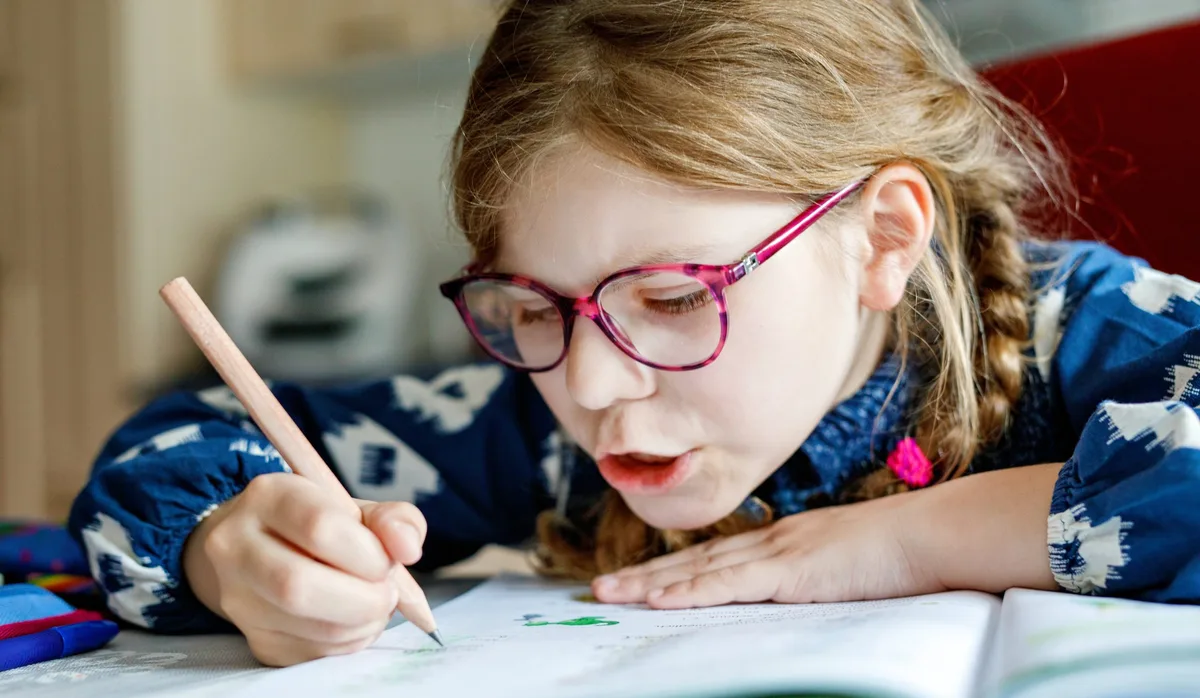Cute elementary school girl sitting at a desk at home, writing in her workbook and doing school homework. Focused child learning and studying indoors. Concept of education, childhood, home learning. Motivation oder Erfolg: Was kommt zuerst?