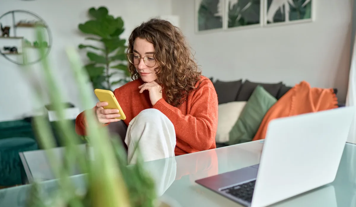Young smiling woman using mobile phone holding cellphone at home. Schnuppern, Berufswahl: Teenager sucht Lehrstelle